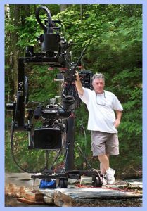 Man posing with a large vintage film camera outdoors.