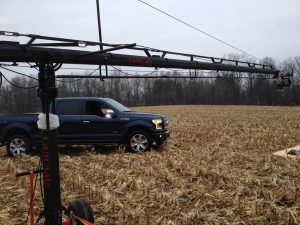 A dark blue truck stuck in a muddy field with farming equipment nearby.