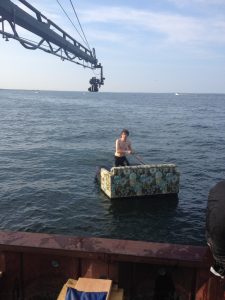Person sitting on a floating platform in the sea with a crane overhead.