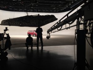 Silhouettes filming a red car in a studio with large equipment.